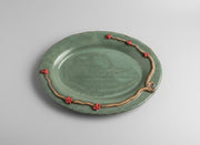 teal ceramic platter with decorative handle and red wintergreen berries on a light background