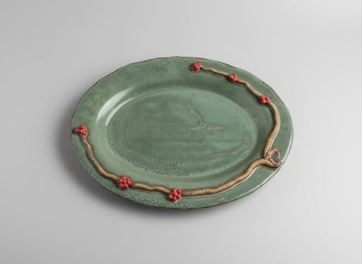 teal ceramic platter with decorative handle and red wintergreen berries on a light background