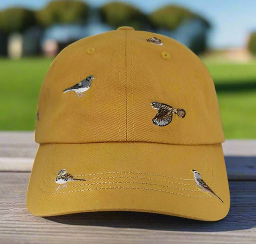 Sparrow Hat - Yellow cap with bird designs on a wooden surface with a blurred green background