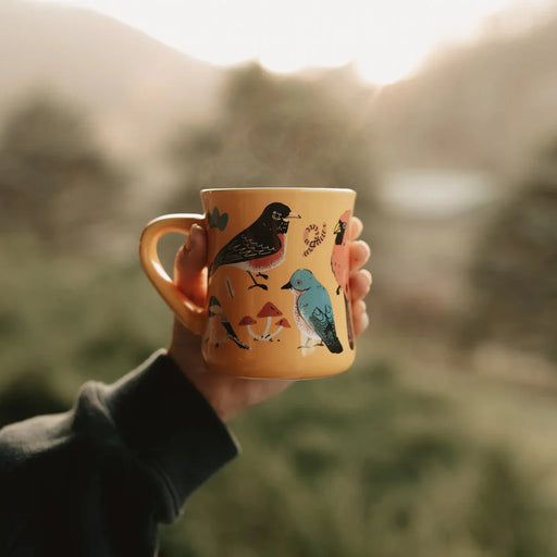 Eastern Backyard Birds Ceramic Mug - Hand holding a mug with bird illustrations against a blurred natural background