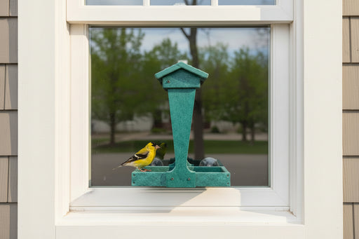 Green Melody Window Mount bird Feeder installed on the exterior of a house window, visited by an American Goldfinch