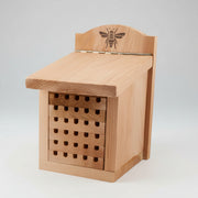 A Heavy Duty Cedar Mason Bee House with a wooden roof, bee logo on the top, and a series of holes in the front panel for entry/exit